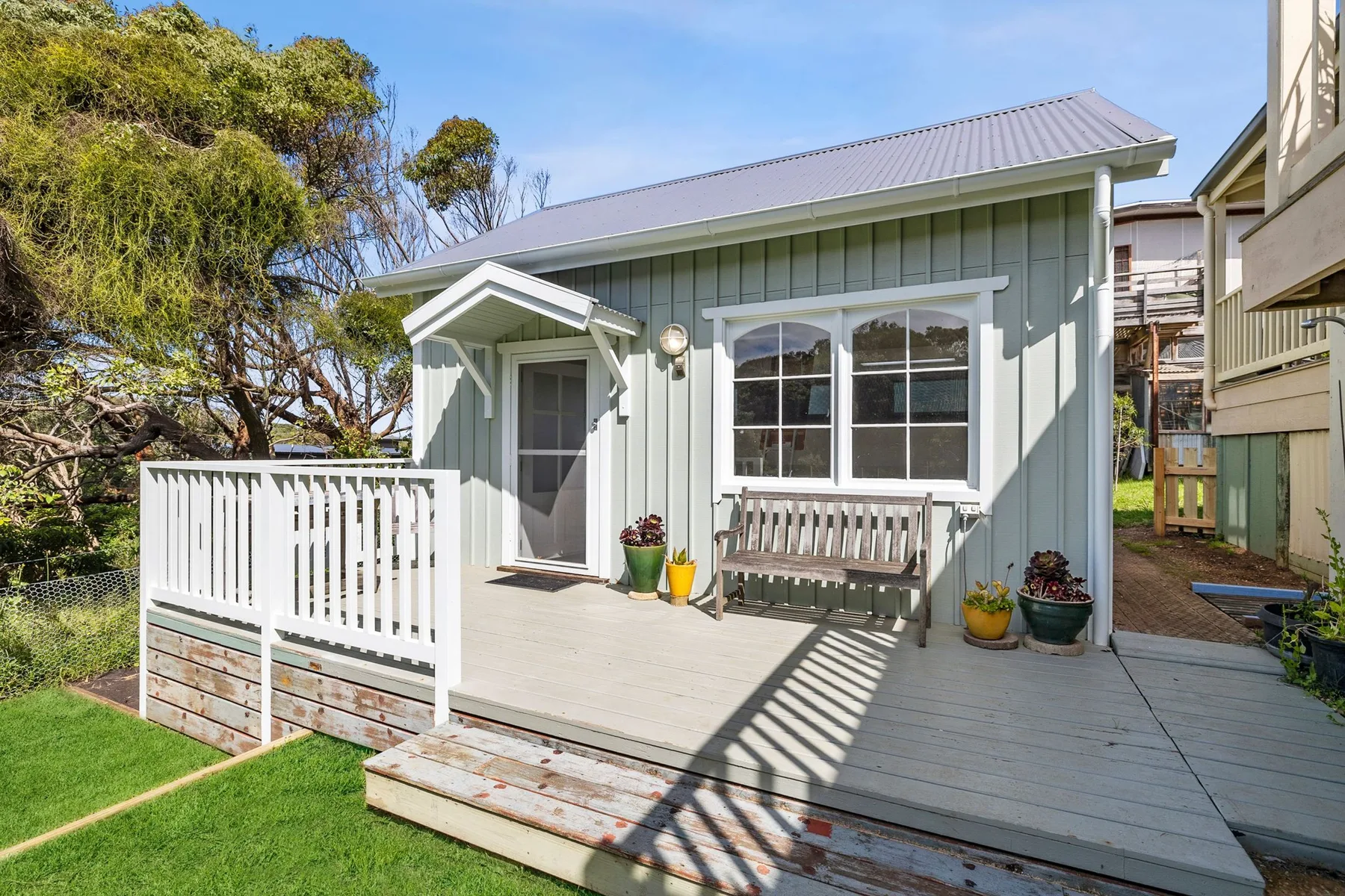 A small house with a raised wooden deck, railing, and outdoor seating.