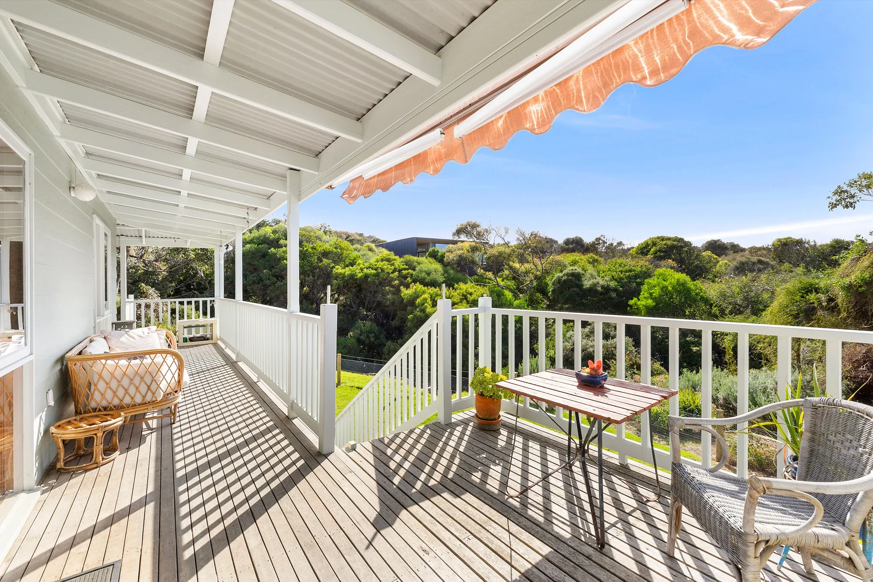 A covered wooden deck with outdoor seating overlooks a green, tree-covered landscape.