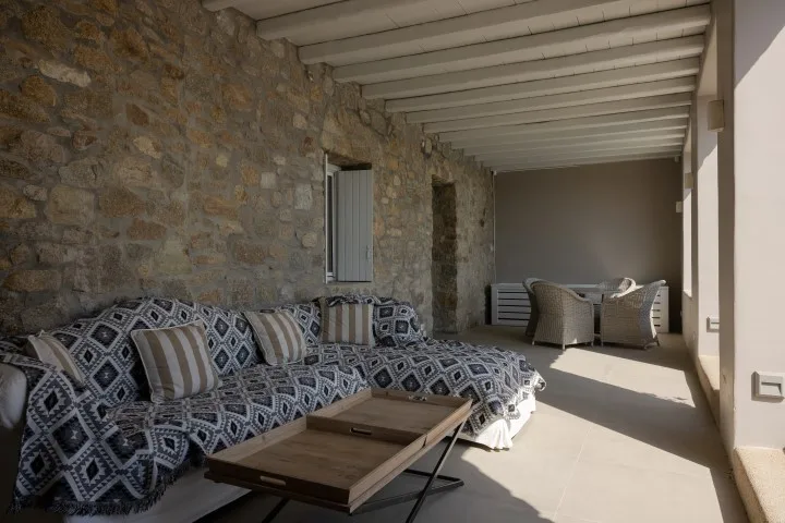 A covered stone-walled patio with patterned seating and a low table.