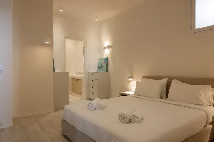 A bedroom with a neatly made bed and a dresser beside the bathroom doorway.