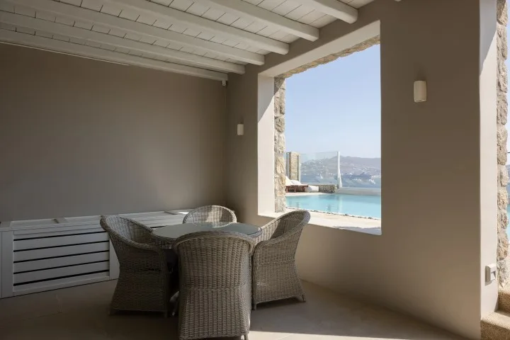 A covered patio with woven seating overlooks a pool and distant water.