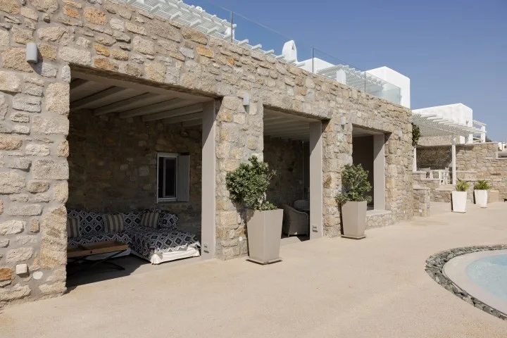 A stone patio with shaded seating and potted plants beside a pool.