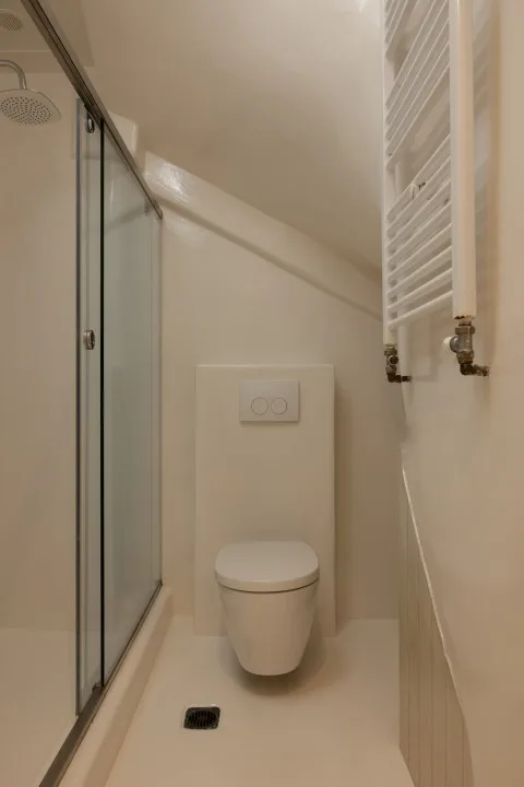 A compact bathroom with a shower, wall-mounted toilet, and radiator.