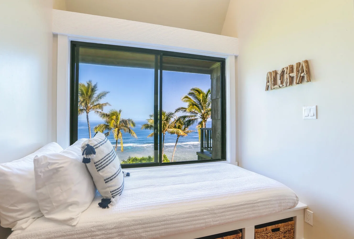 Un dormitorio con una cama frente a una ventana amplia con palmeras y el mar a la vista.