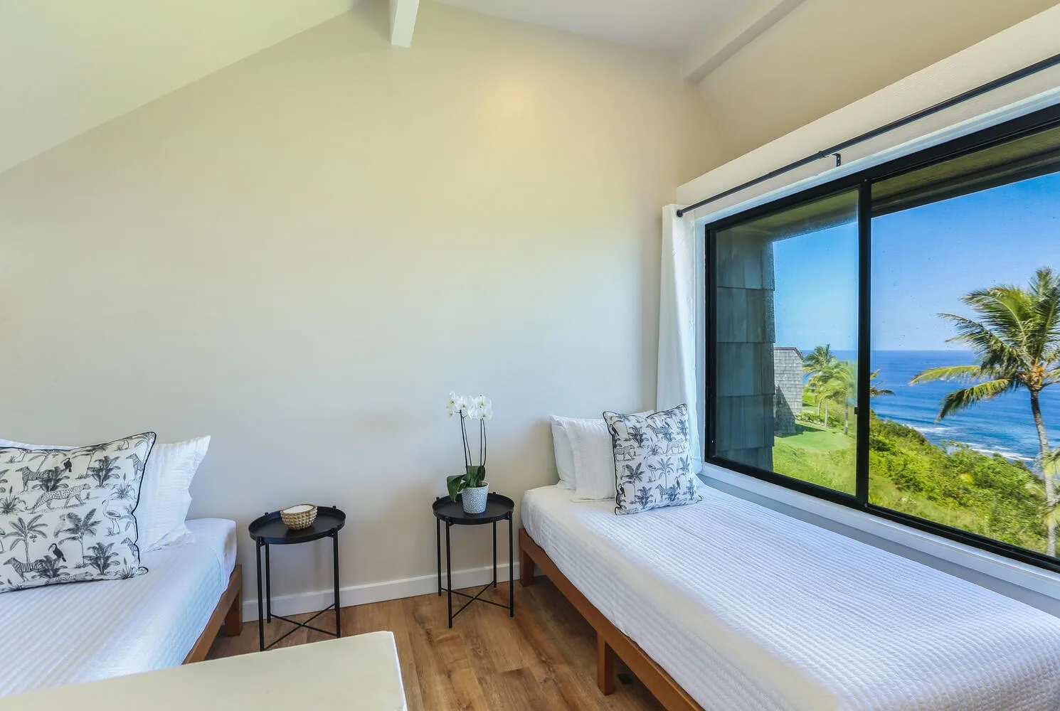 Un dormitorio luminoso tiene dos camas junto a una ventana grande con vistas al mar.