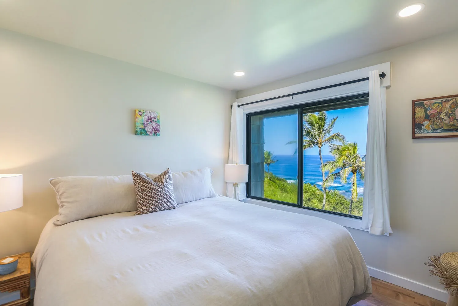 Un dormitorio luminoso con una cama grande junto a una puerta corrediza de vidrio con vista al mar.