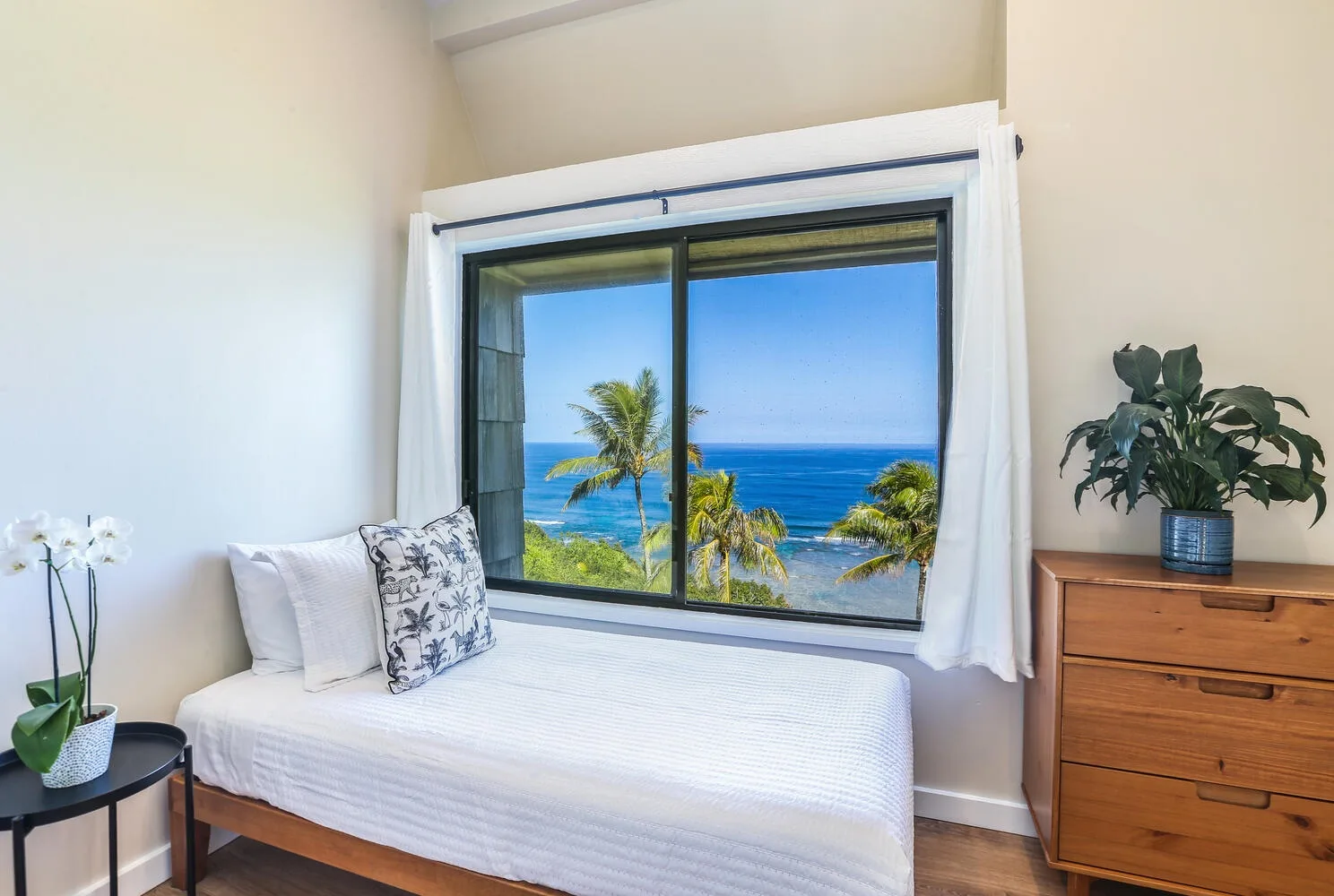 Un dormitorio con una cama junto a una ventana grande con vistas al océano.