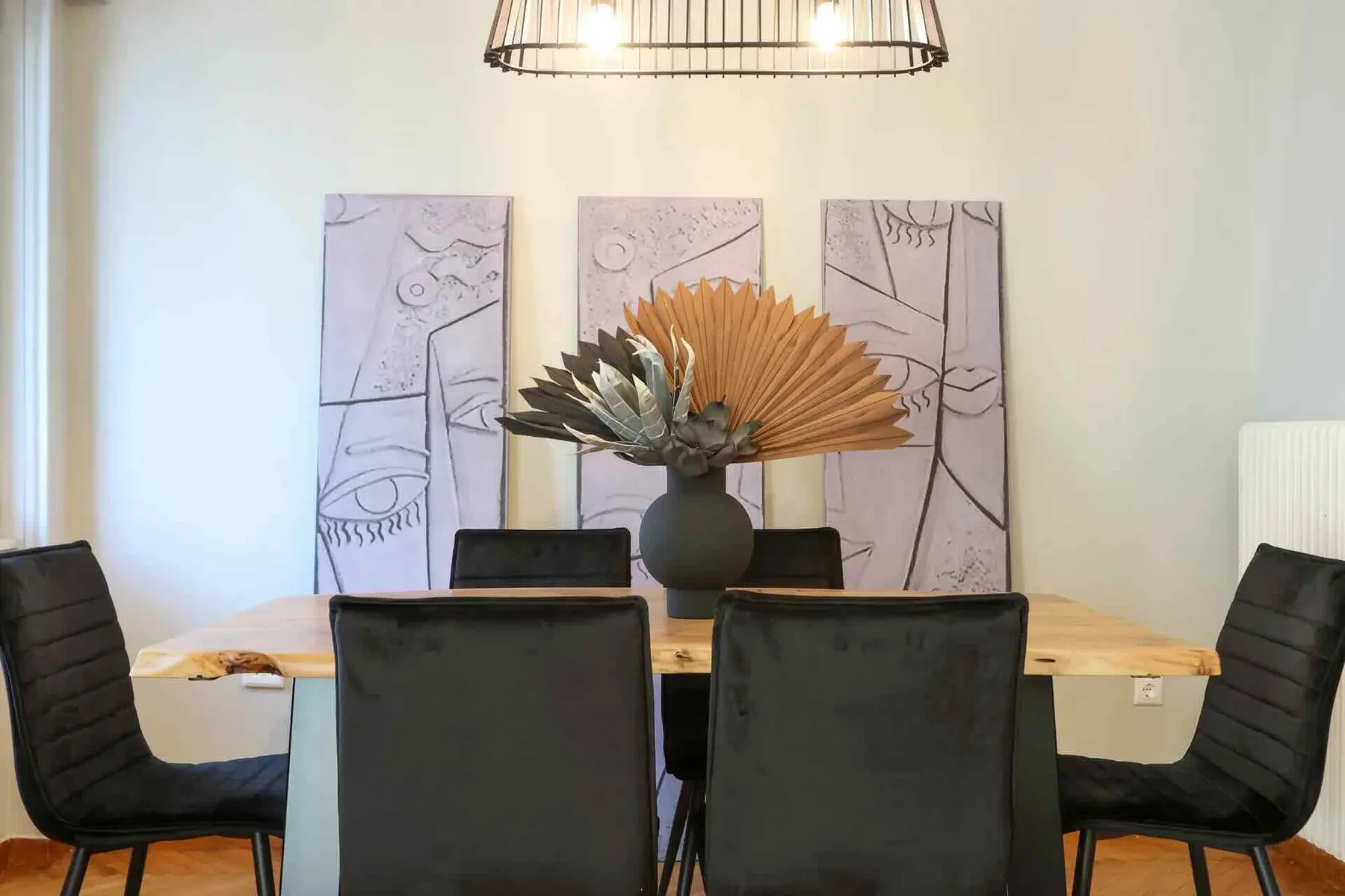 Un comedor cuenta con una mesa de madera, asientos oscuros y arte abstracto en la pared.