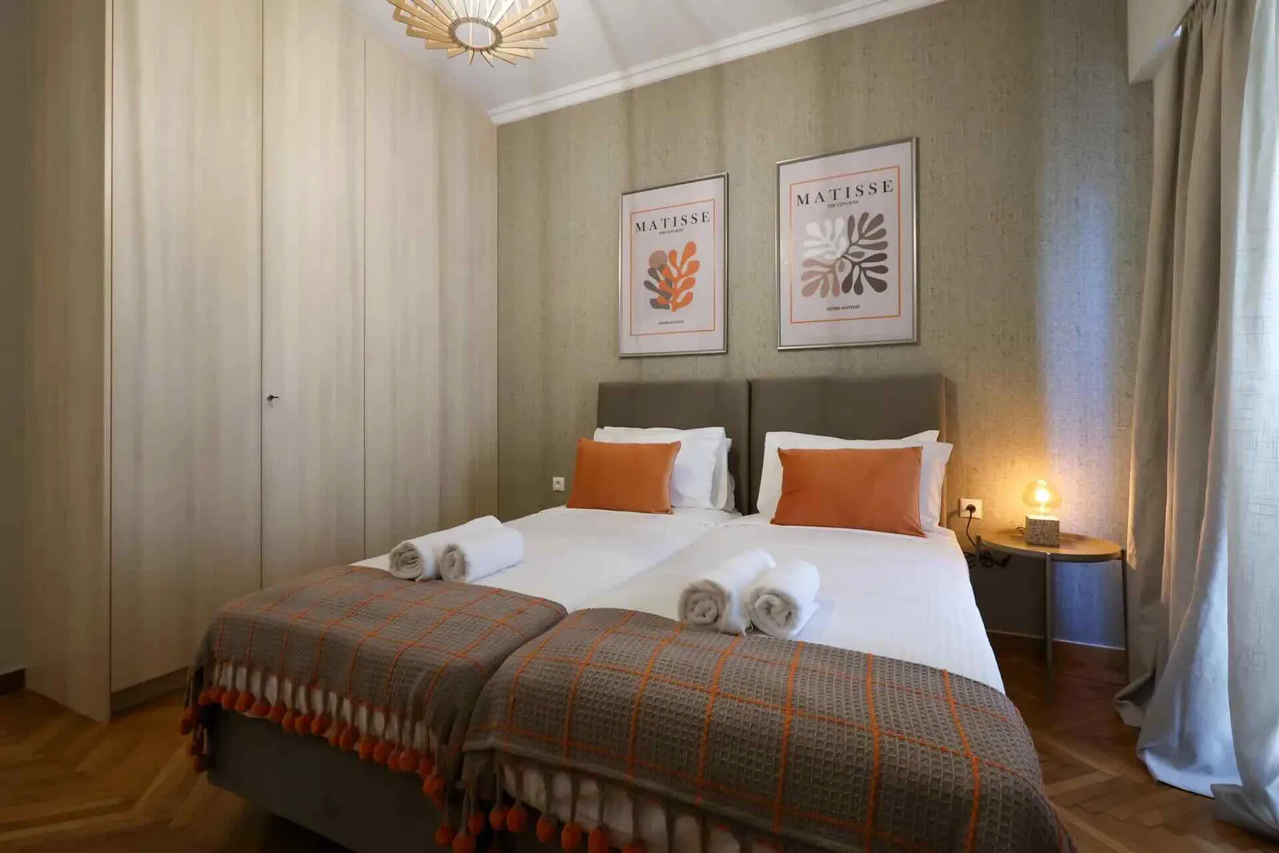 Un dormitorio con una cama doble, cojines naranjas y láminas botánicas enmarcadas.