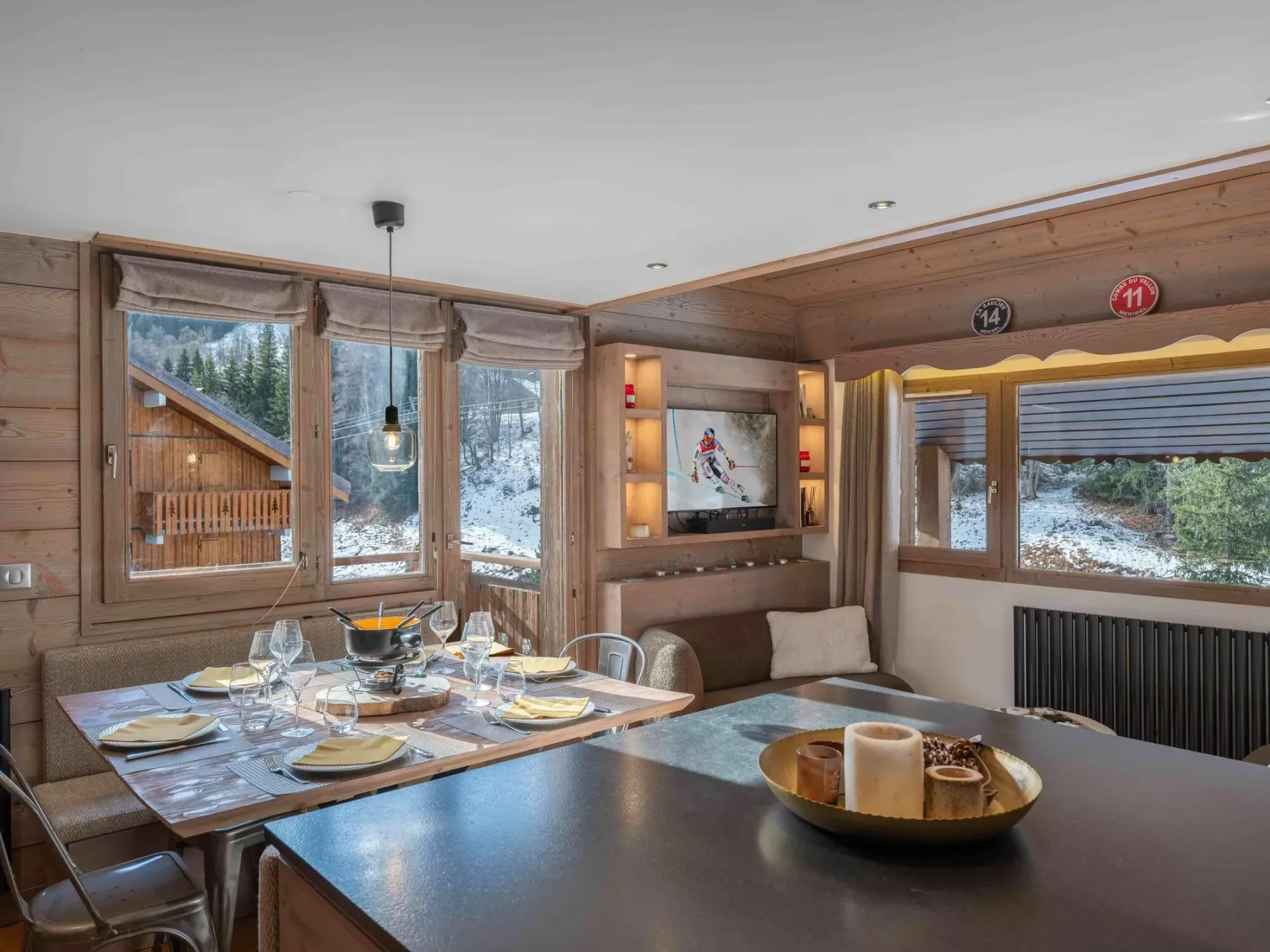 A wood-paneled dining area has a set table beside windows overlooking a snowy landscape.