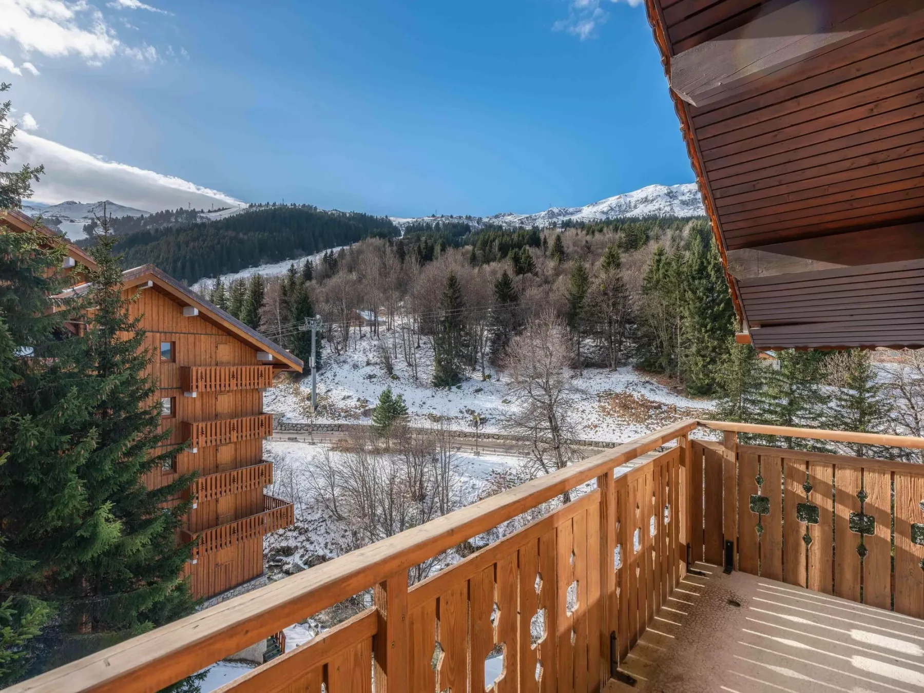 A wooden balcony overlooks a snow-dusted mountain valley beneath a clear blue sky.