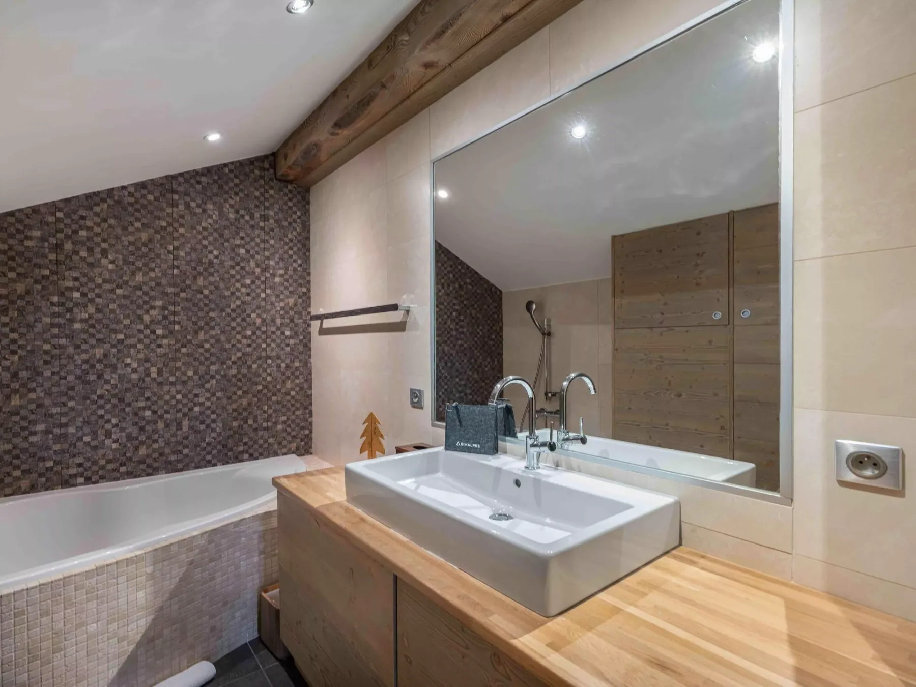 A bathroom with a wide sink vanity and a bathtub beside a tiled wall.