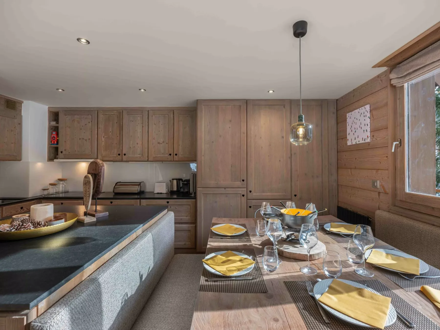 A dining area with a set table beside a kitchen with wooden cabinets.