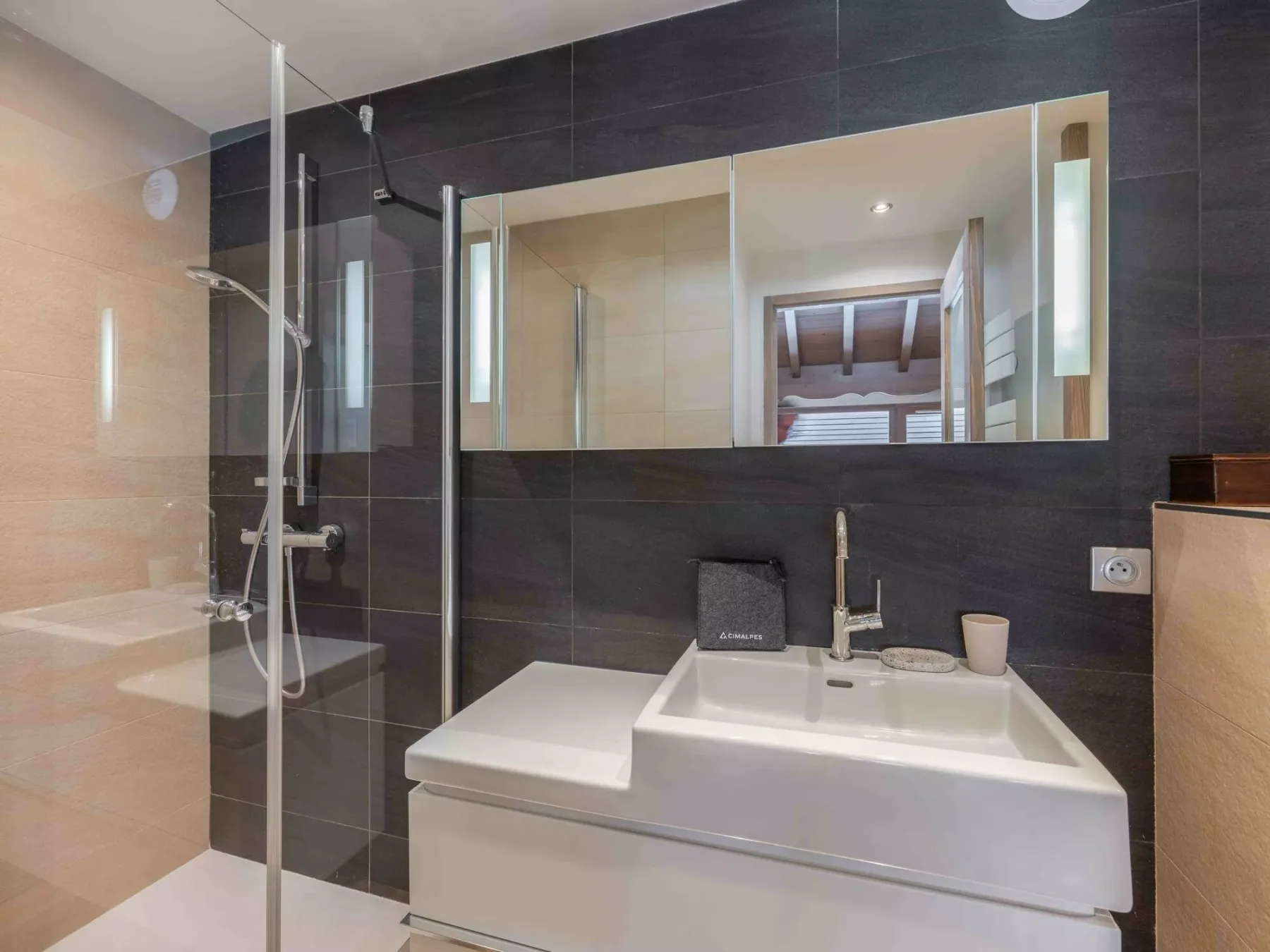 A bathroom with a sink, wide mirror, and glass shower screen.