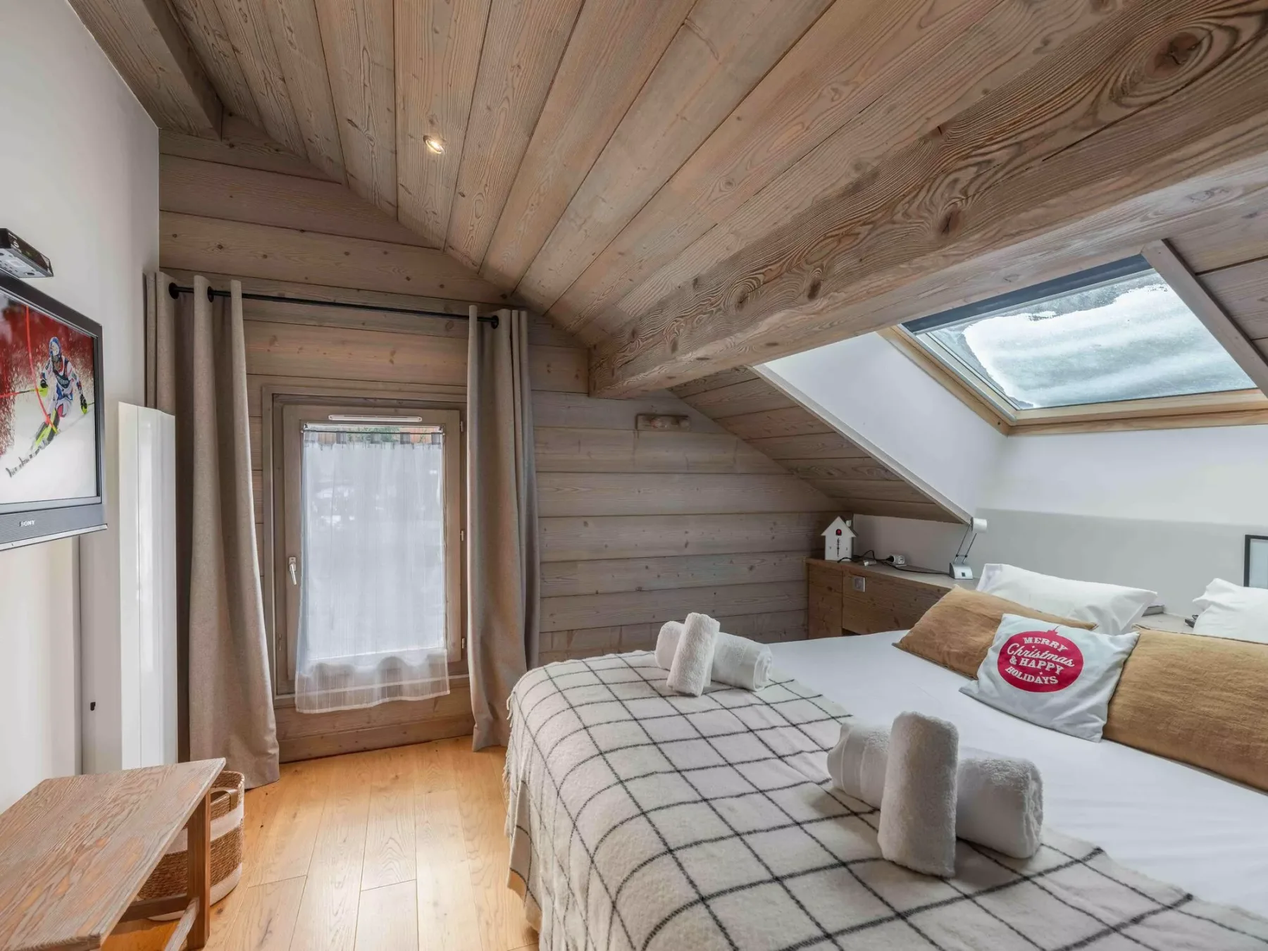 A bedroom with a bed beneath a sloped wooden ceiling and skylight.