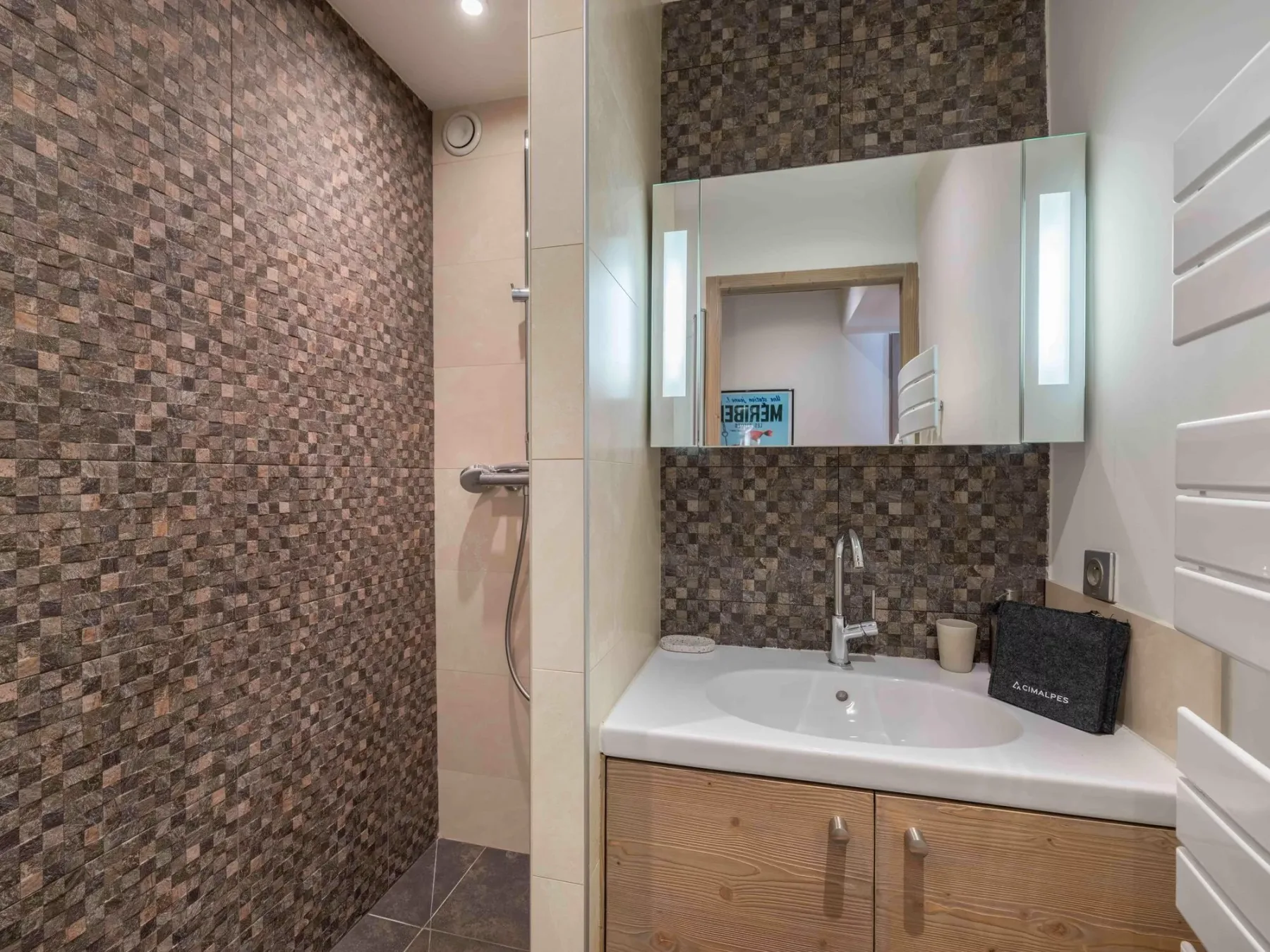 A bathroom with a sink beneath a wall mirror and a tiled shower area.