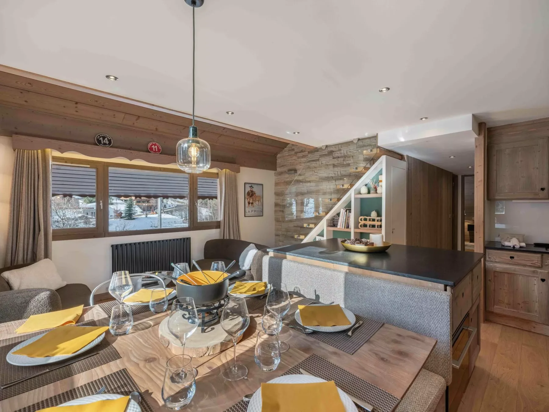 A dining area with a set table sits beside a kitchen counter and stone wall.