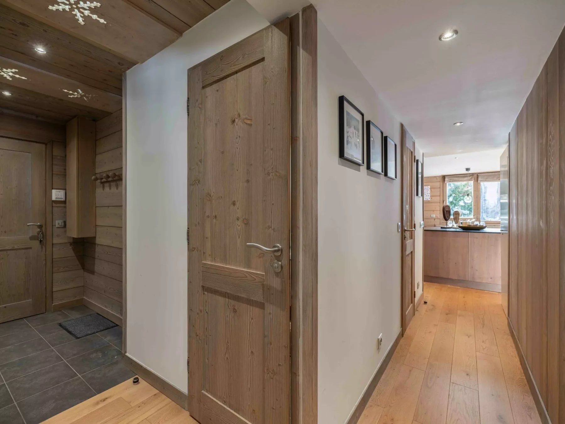 A wood-paneled entryway opens onto a hallway leading to a kitchen.
