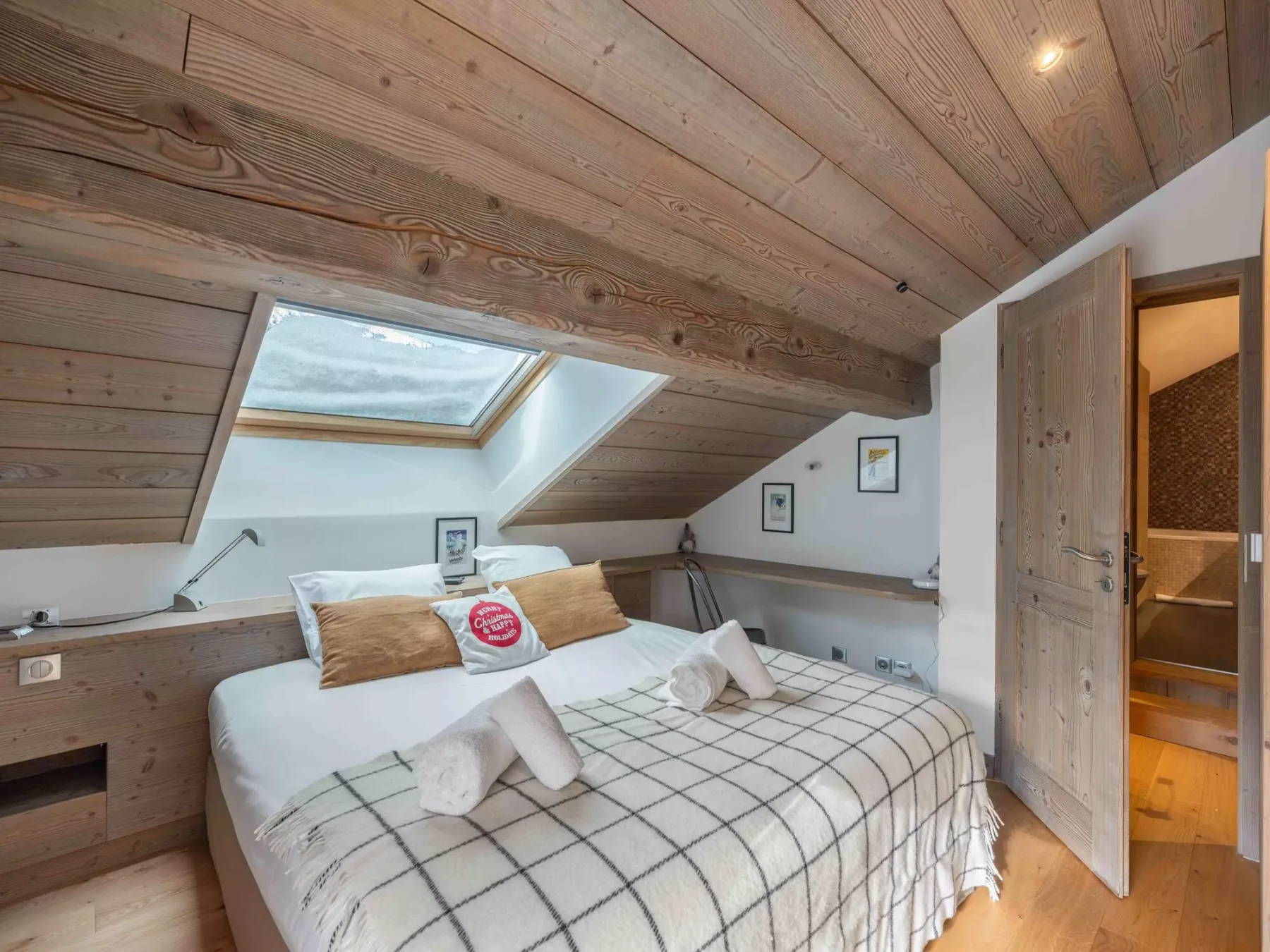 A bedroom with a bed beneath a sloped wooden ceiling and skylight.