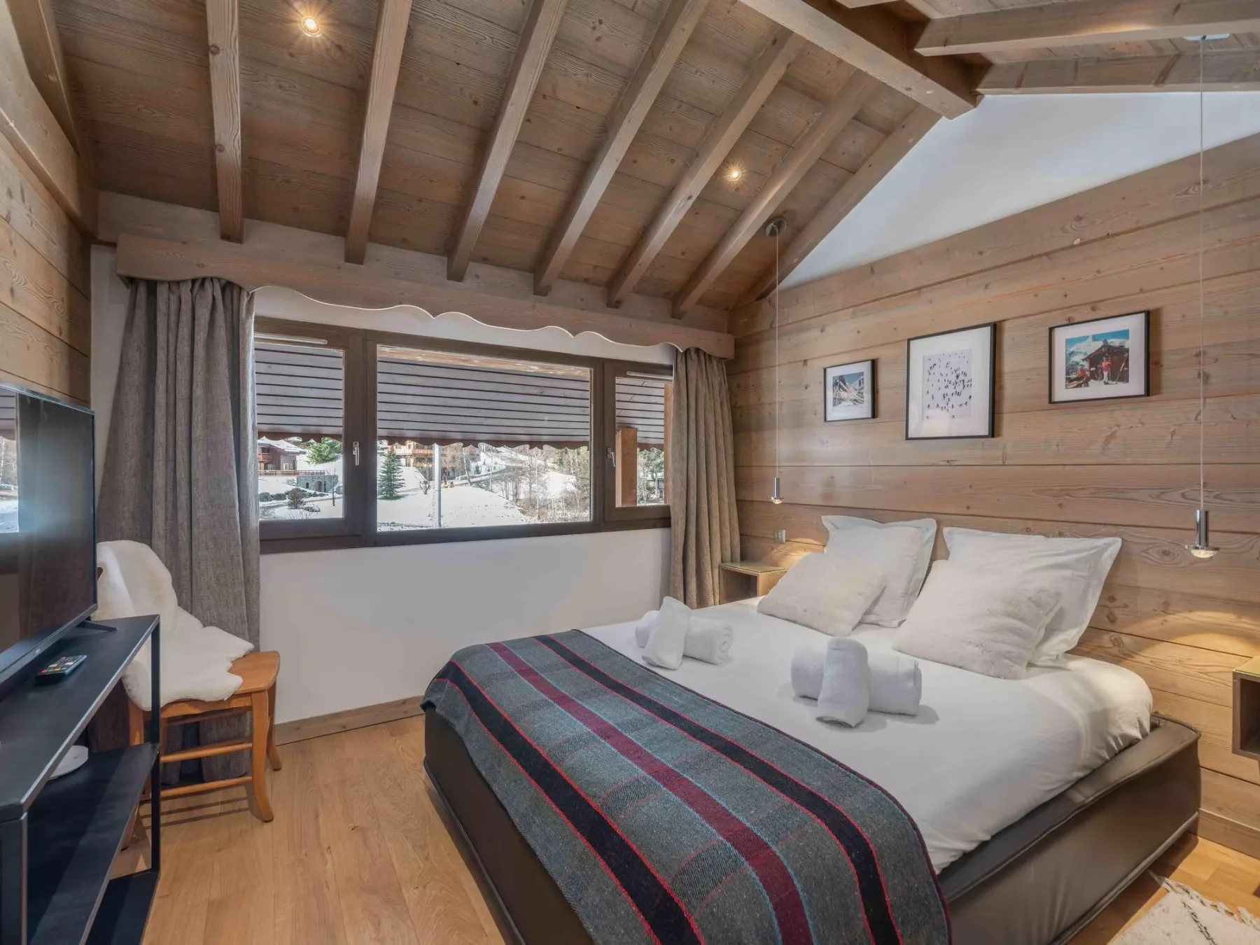 A bedroom with a large bed, wood-paneled walls, and a sloped timber ceiling.