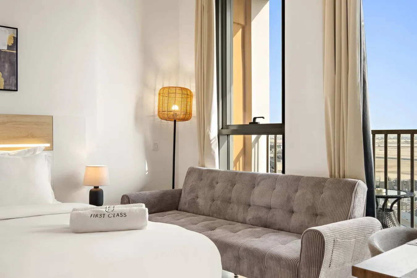 A bright bedroom with a bed, a gray sofa, and tall windows.