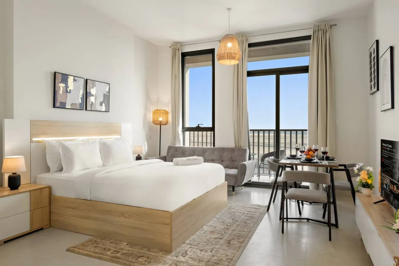 A bright bedroom with a large bed, seating area, and glass doors opening to a balcony.