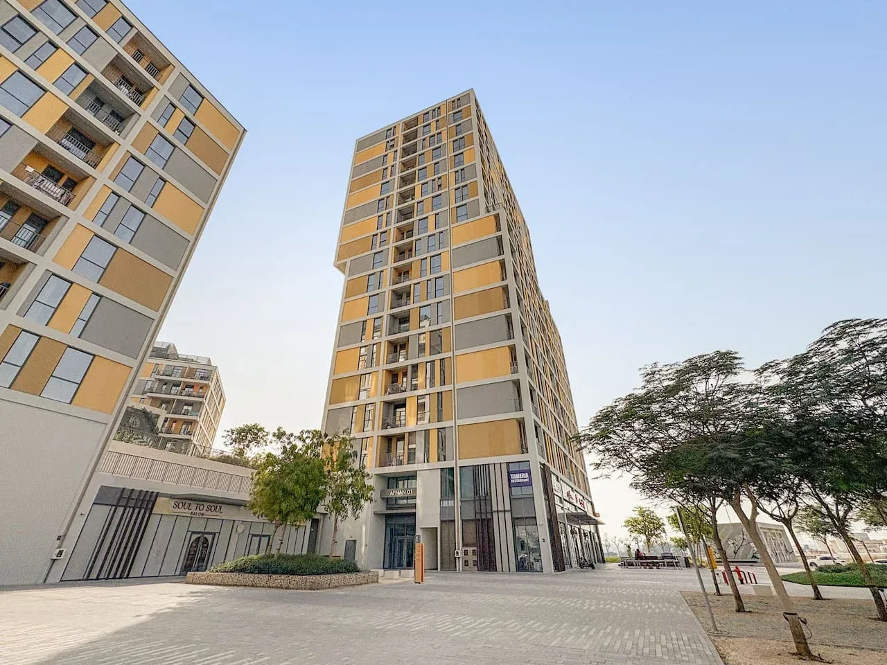 A paved plaza sits between modern apartment buildings and leafy trees.
