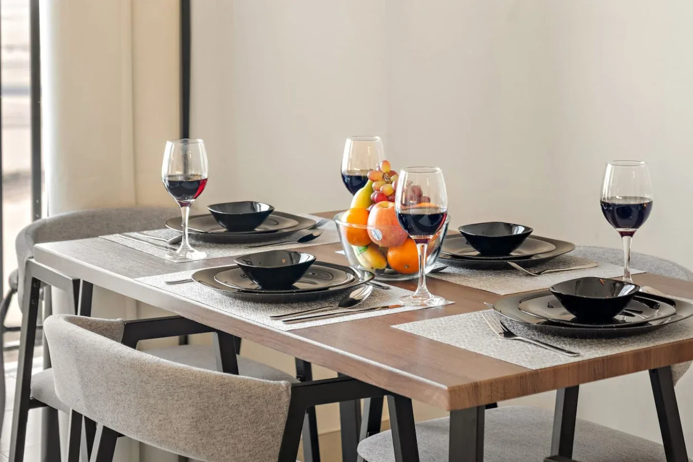 A dining table is set with plates, glasses of wine, and a bowl of fruit.