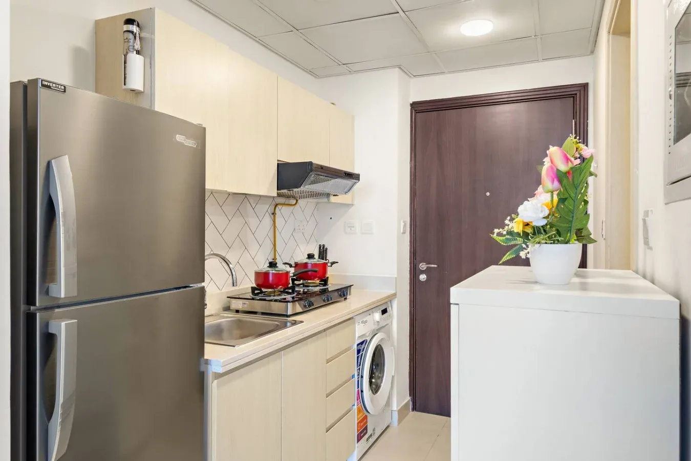 A compact kitchen with a refrigerator, stovetop, and washing machine.