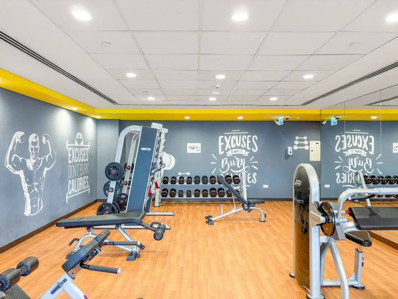 A gym with weight machines and exercise equipment on a wood-colored floor.