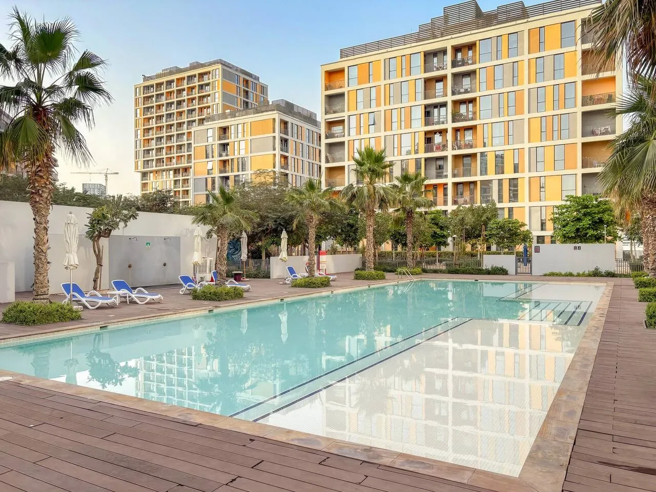 An outdoor swimming pool sits in front of modern apartment buildings and palm trees.