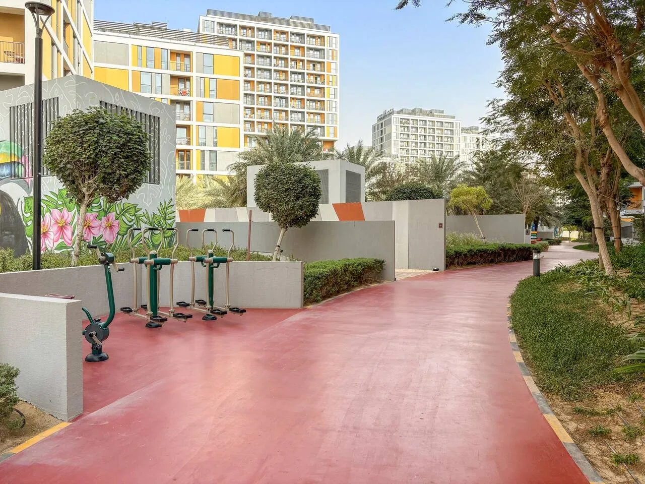 A red paved walkway runs past outdoor exercise equipment and landscaped grounds.