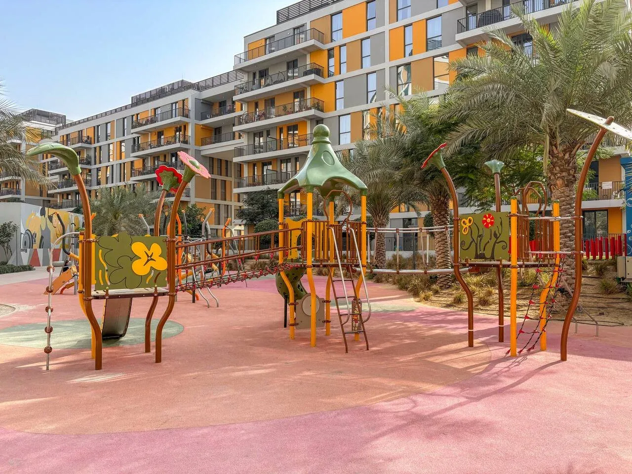 A colorful outdoor playground with climbing structures and apartment buildings in the background.