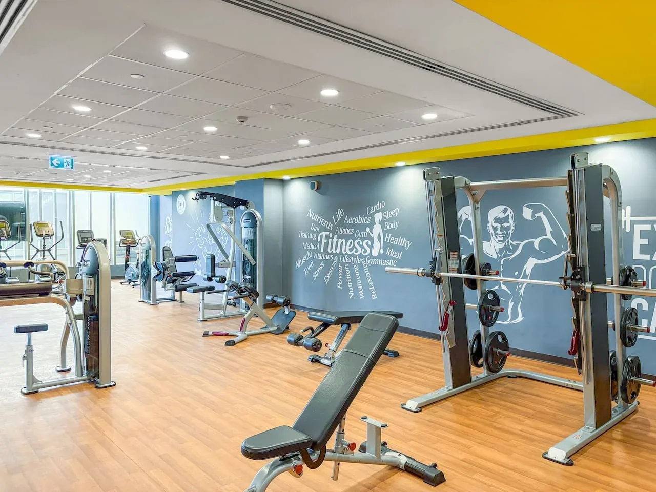 A gym with weight machines and benches arranged across a bright exercise room.