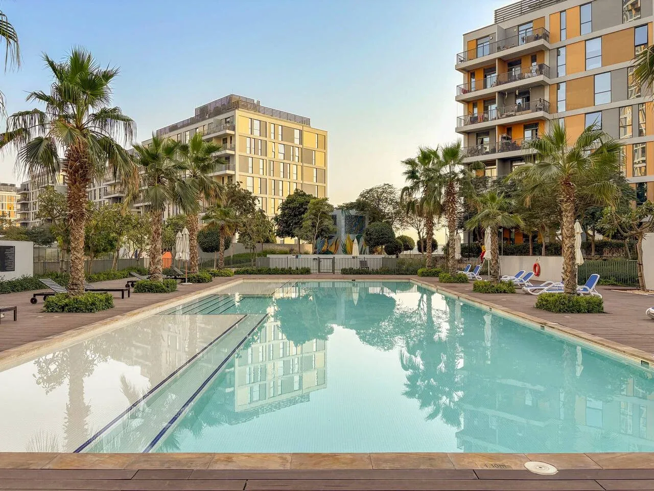 An outdoor swimming pool sits among palm trees and apartment buildings.