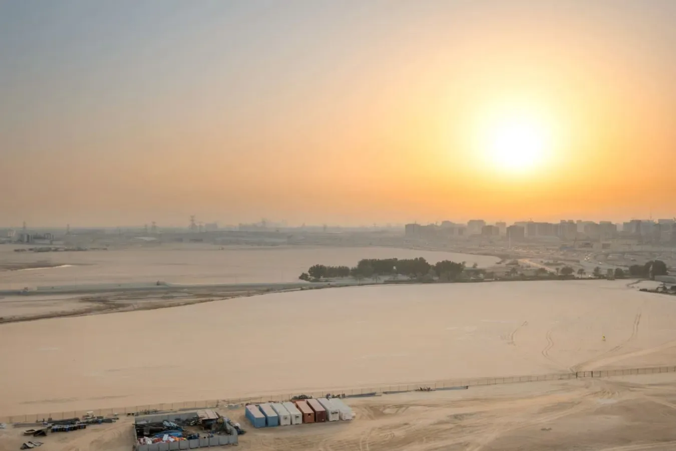A sunset over a broad sandy shoreline with a distant city skyline.