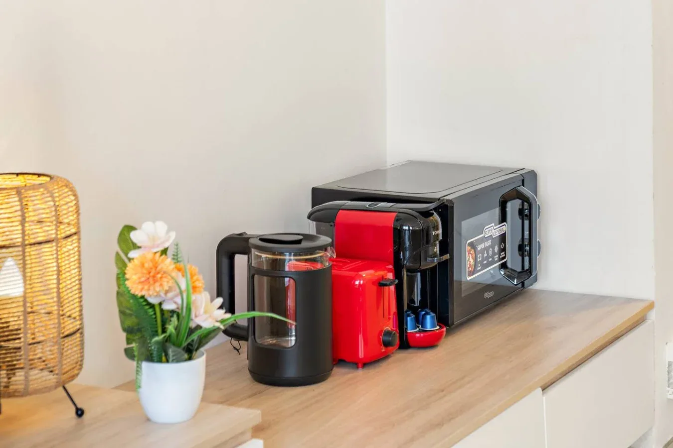 A countertop coffee station with a coffee maker, red coffee machine, and flowers.