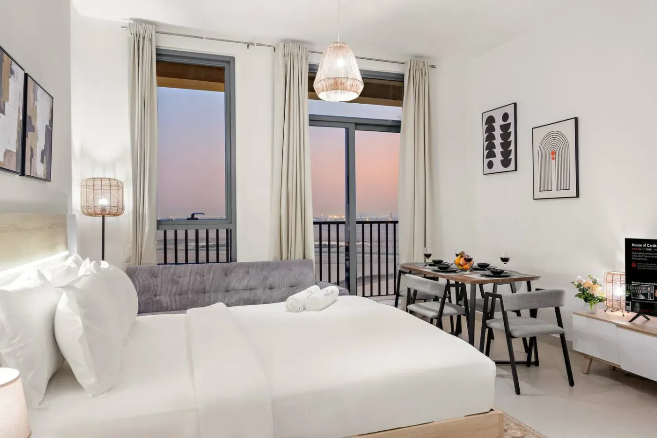 A bedroom with a large bed, dining table, and balcony doors.