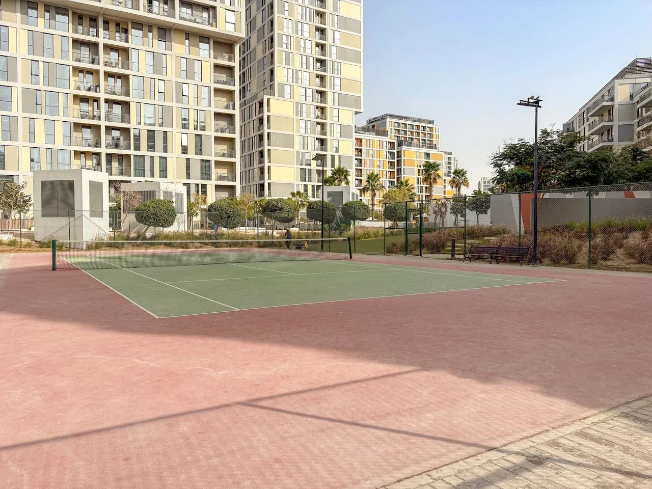 An outdoor tennis court sits in front of modern apartment buildings.