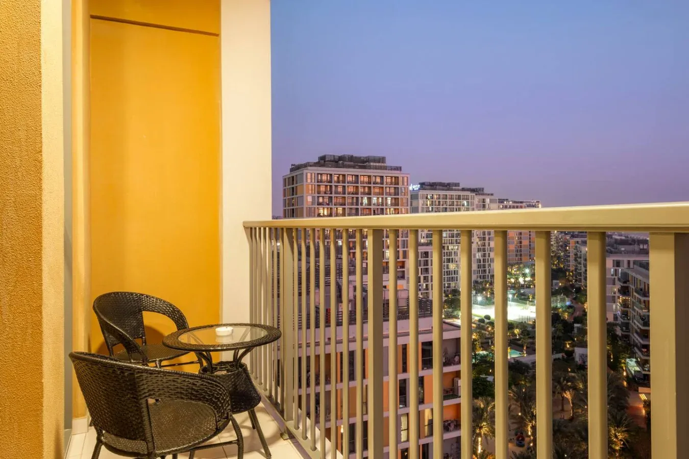 A balcony seating area overlooks illuminated apartment buildings at dusk.