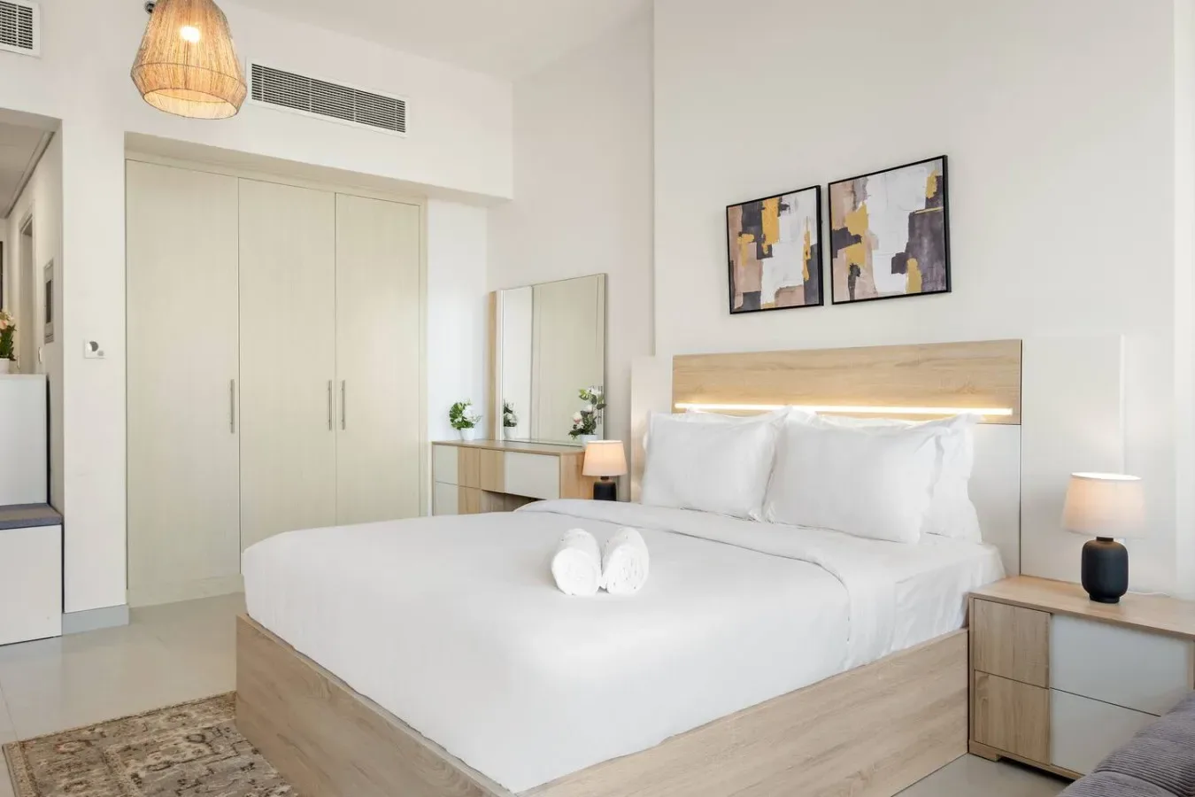 A bright bedroom with a neatly made bed and abstract artwork above the headboard.