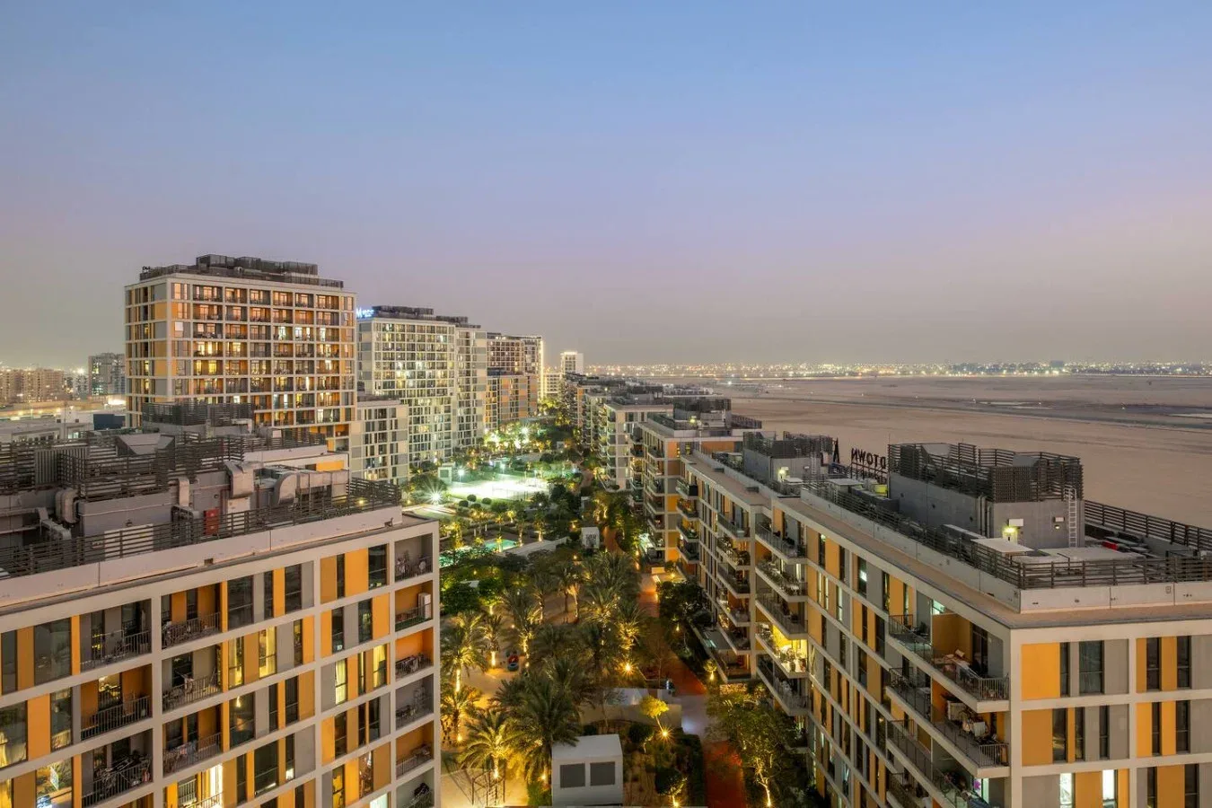 A cityscape at dusk shows modern buildings beside a waterfront.