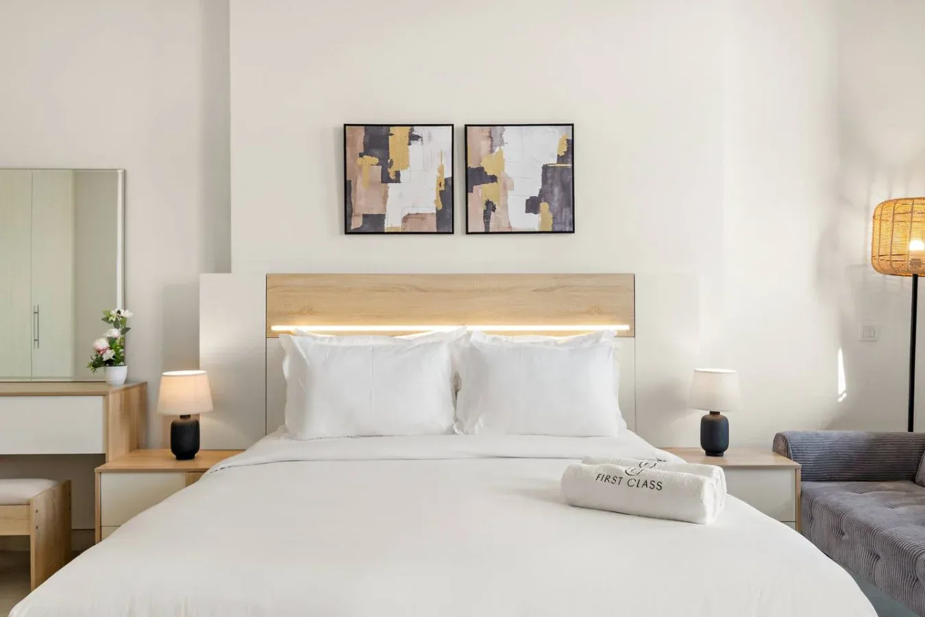 A bright bedroom with a neatly made bed and abstract artwork above the headboard.
