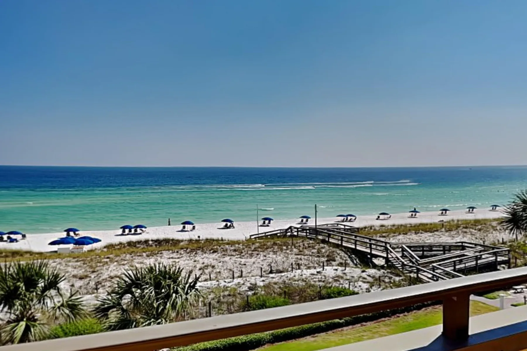 A coastal beach with turquoise water, sandy dunes, and a wooden boardwalk.