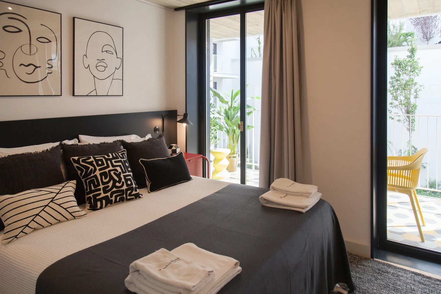 Dormitorio con una cama bien arreglada junto a grandes puertas de vidrio que dan a un balcón.
