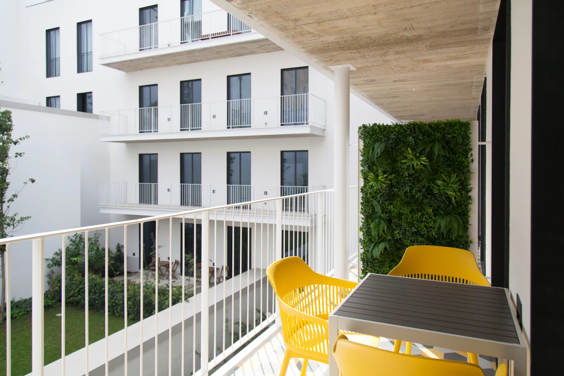 Una zona de estar en un balcón da a un patio con un muro verde.