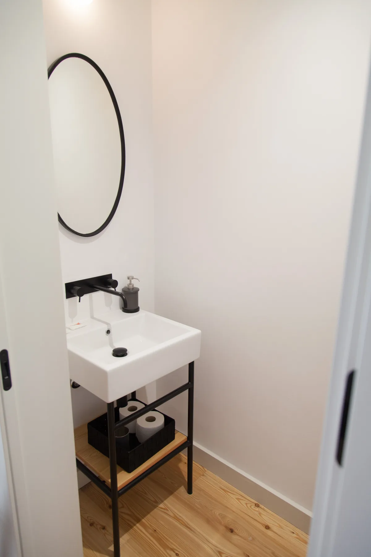Un baño pequeño con lavabo suspendido y espejo redondo.