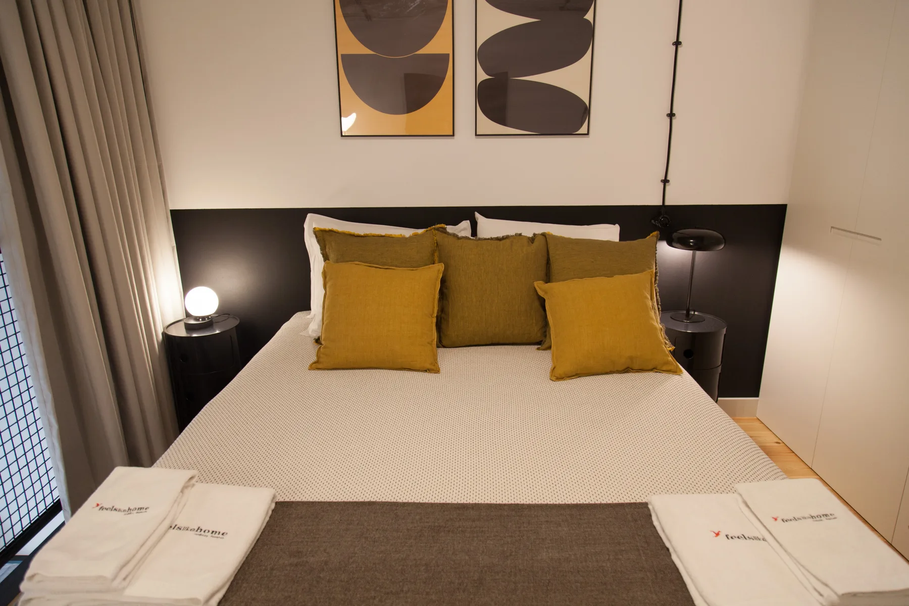 Un dormitorio con una cama, cojines mostaza y arte abstracto en la pared.