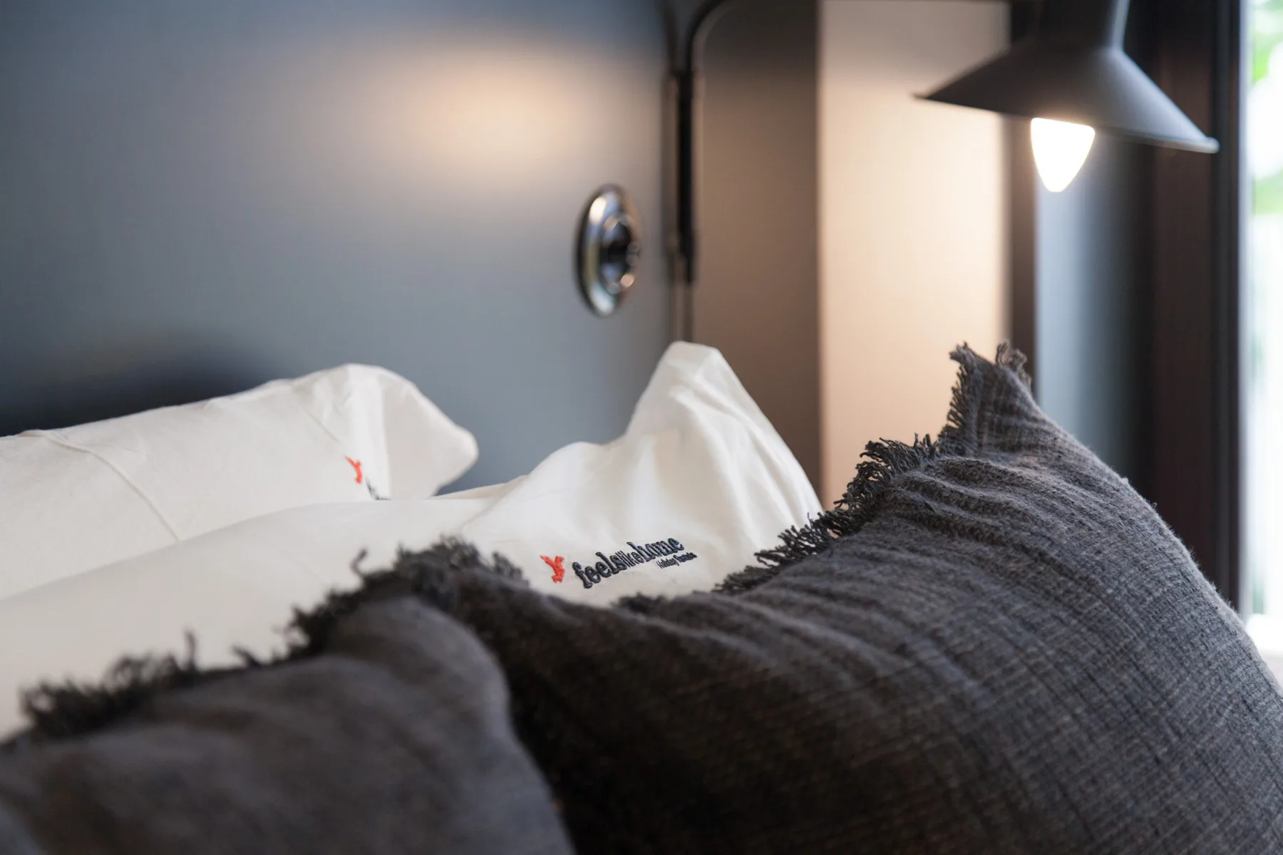 Un dormitorio con almohadas blancas y cojines oscuros sobre la cama.
