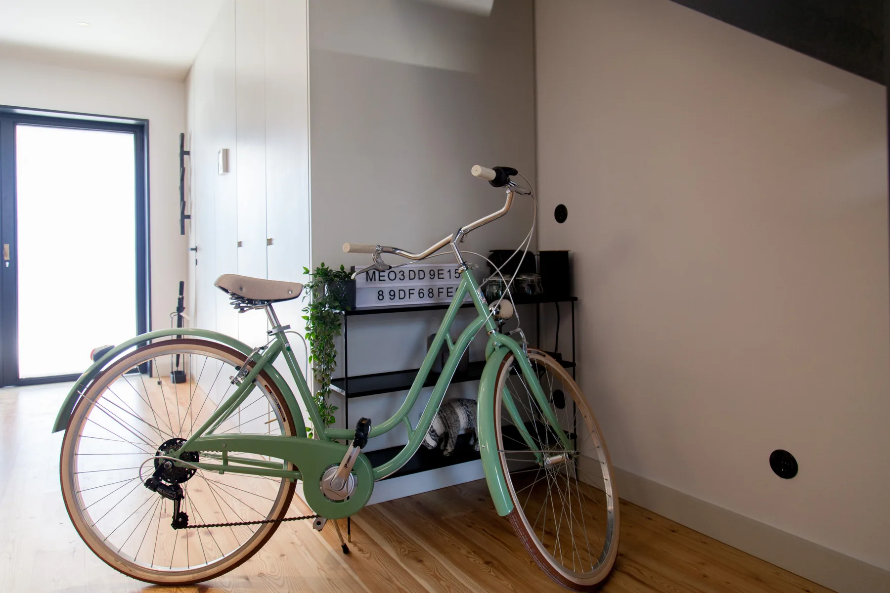 Una bicicleta está junto a una mesa pequeña en una habitación luminosa con suelo de madera.